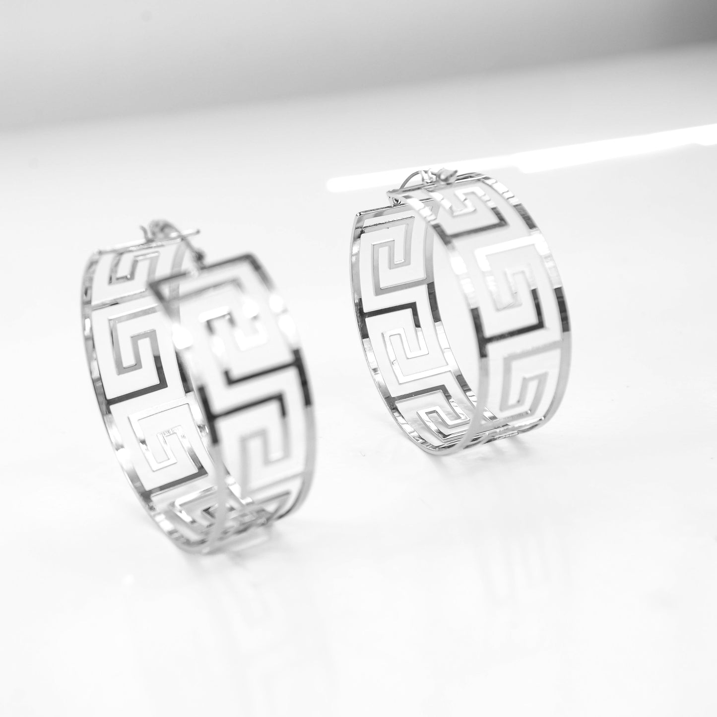 Pair of silver hoop earrings with geometric design on a white background