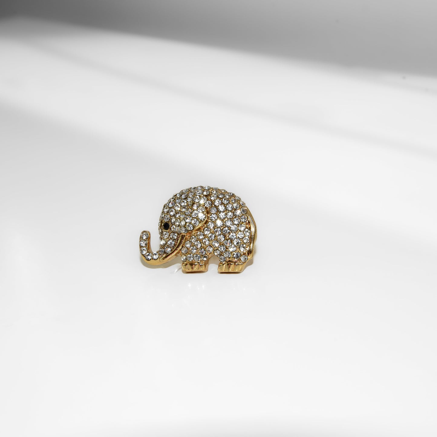 Gold elephant-shaped brooch with gemstones on a white background