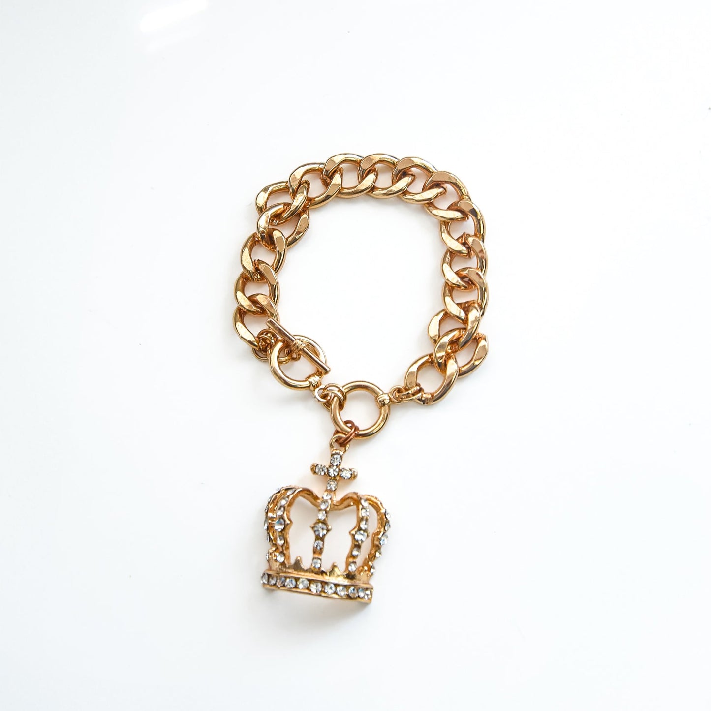 Gold chain bracelet with a crown charm on a white background