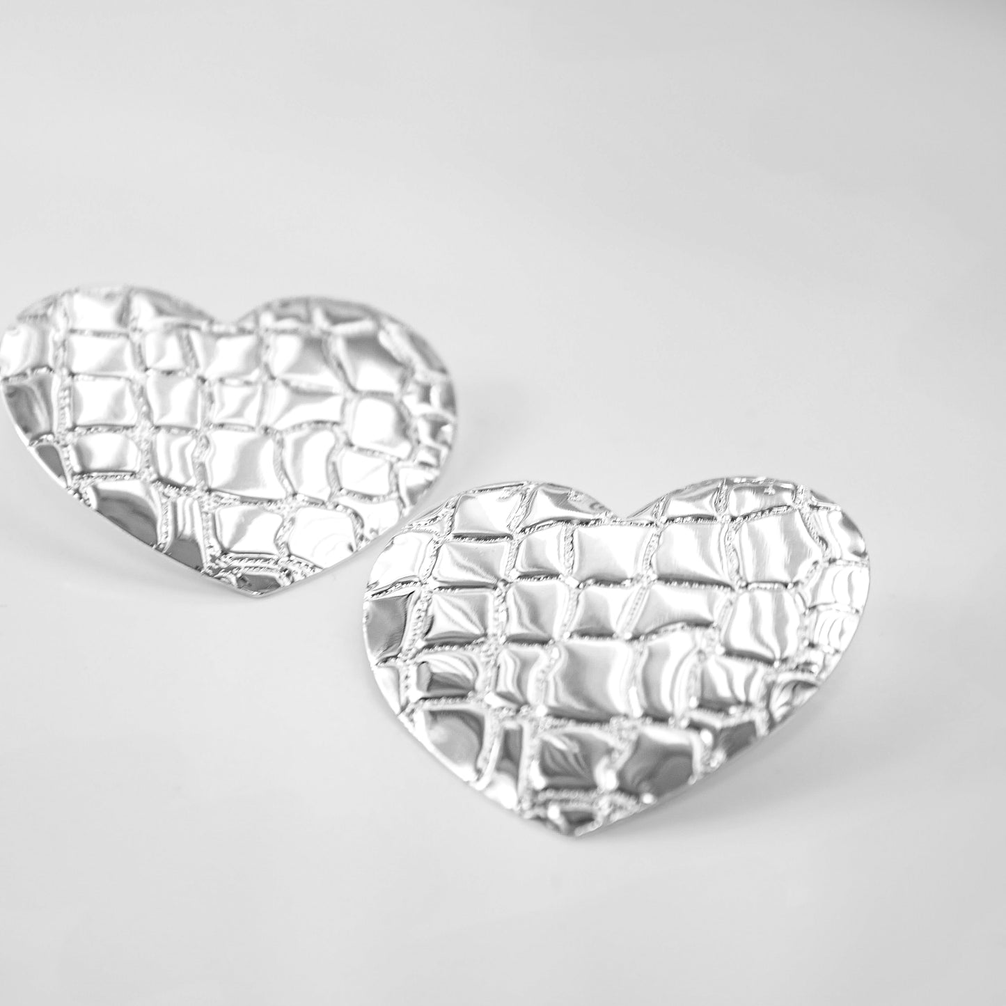 Heart-shaped silver earrings on a light gray background