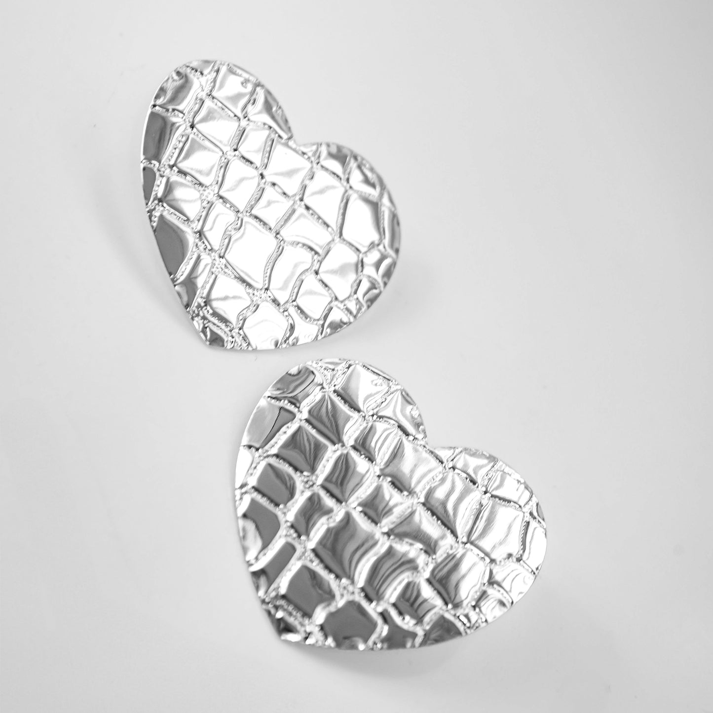 Heart-shaped silver earrings on a light gray background