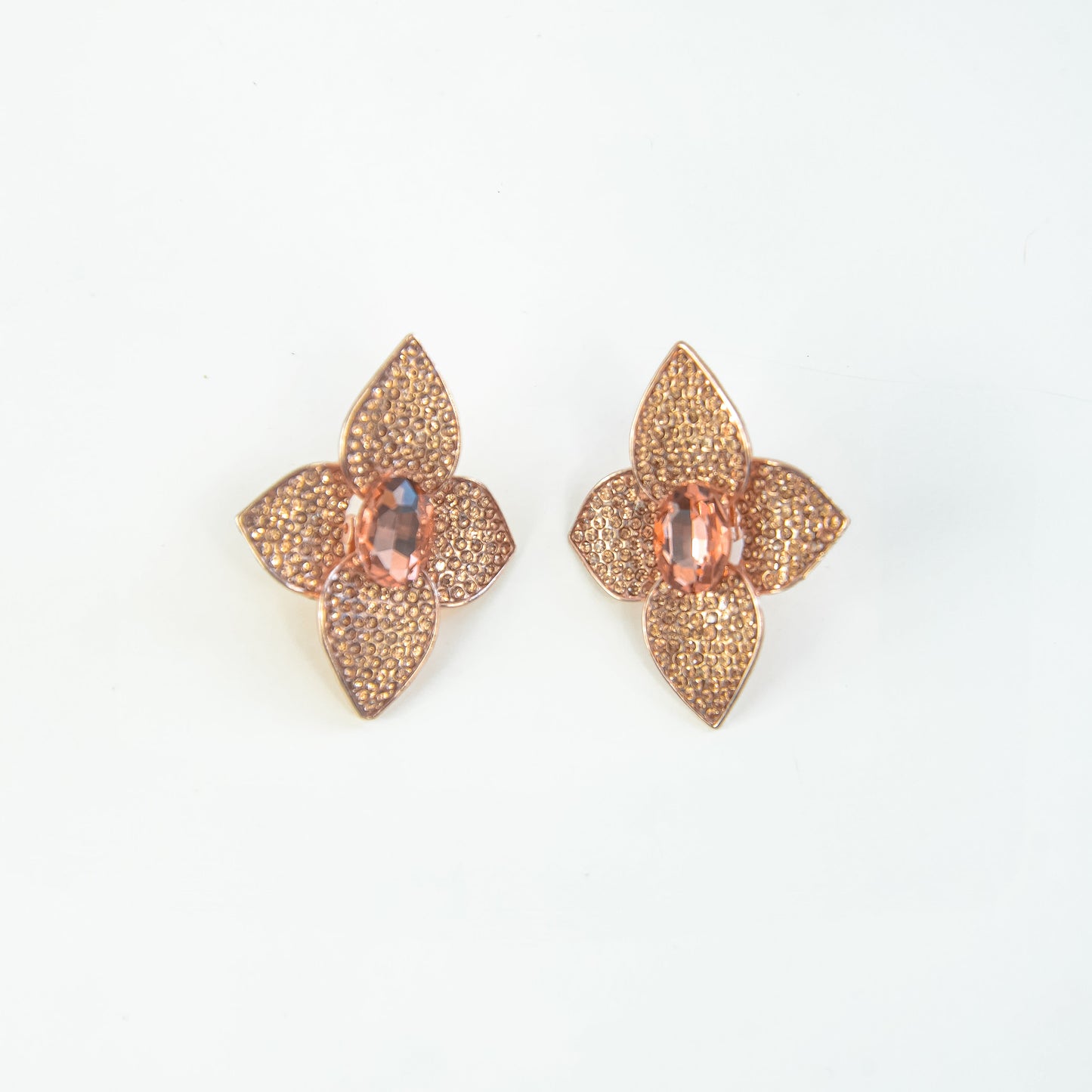 Pair of gold floral earrings with pink gemstones on a light gray background