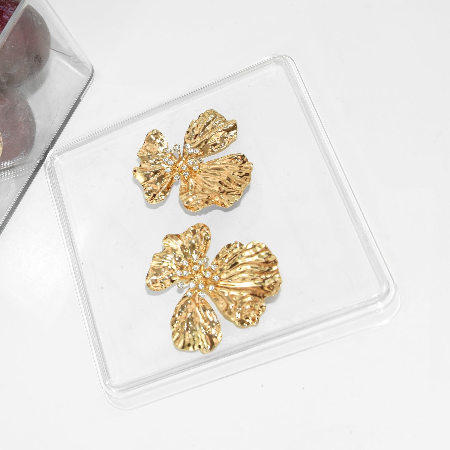 Gold butterfly earrings on a clear stand with plums in the background