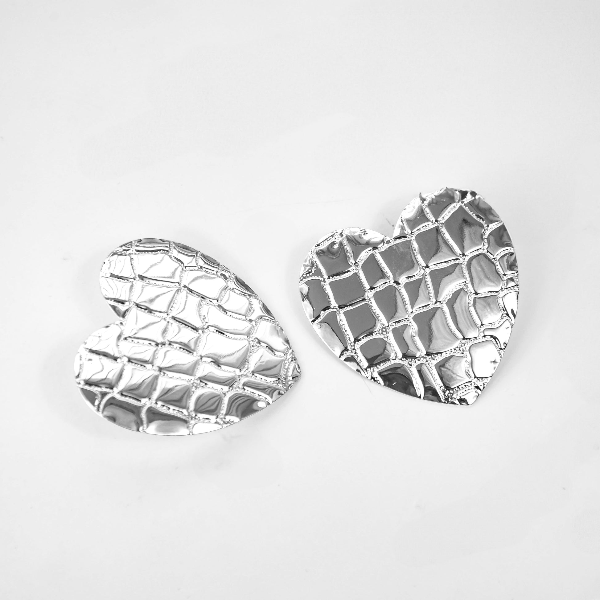 Heart-shaped silver earrings on a light gray background