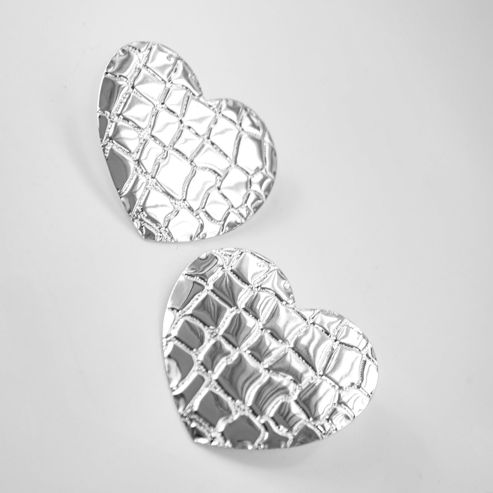 Heart-shaped silver earrings on a light gray background