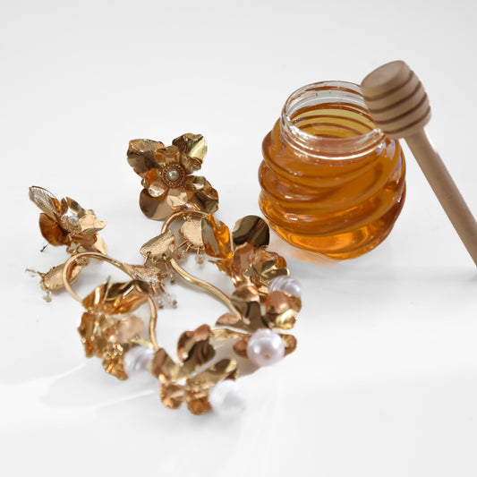 Jar of honey with a wooden dipper and floral earrings on a white background