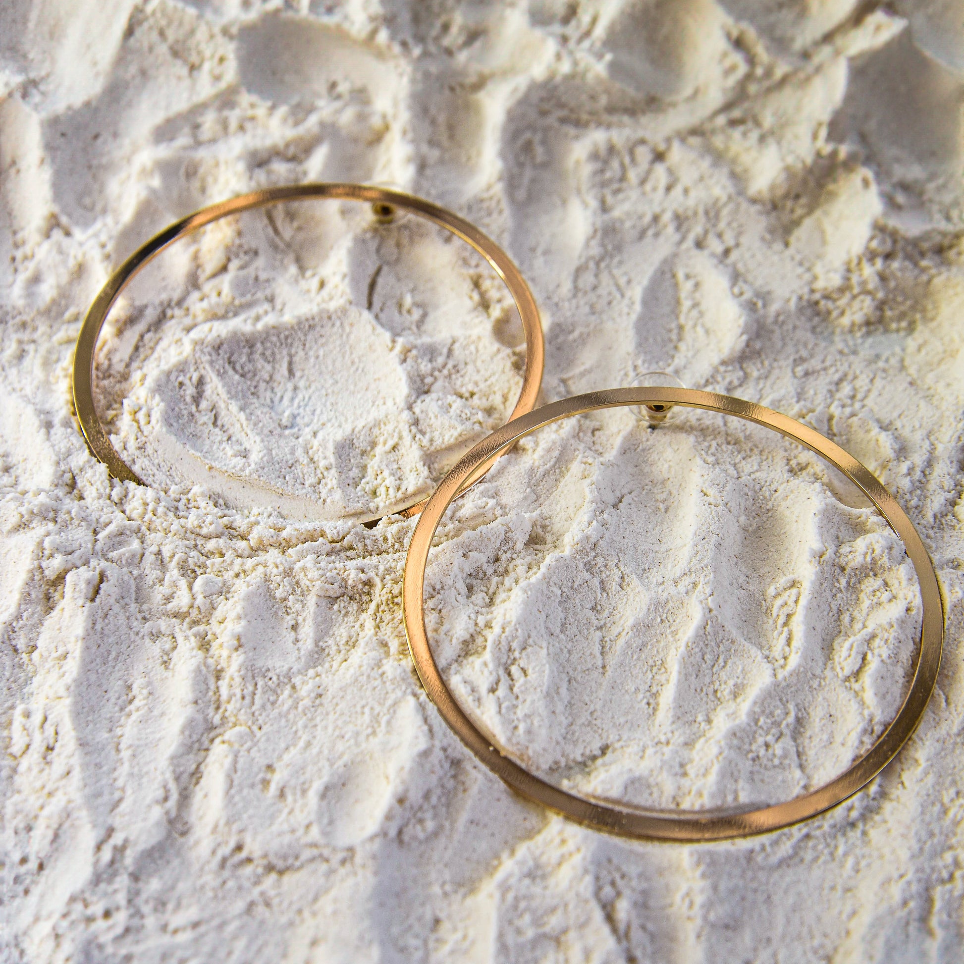 Two gold earrings on a textured beige surface