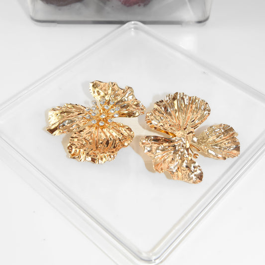 Gold leaf-shaped earrings on a clear stand with a blurred background